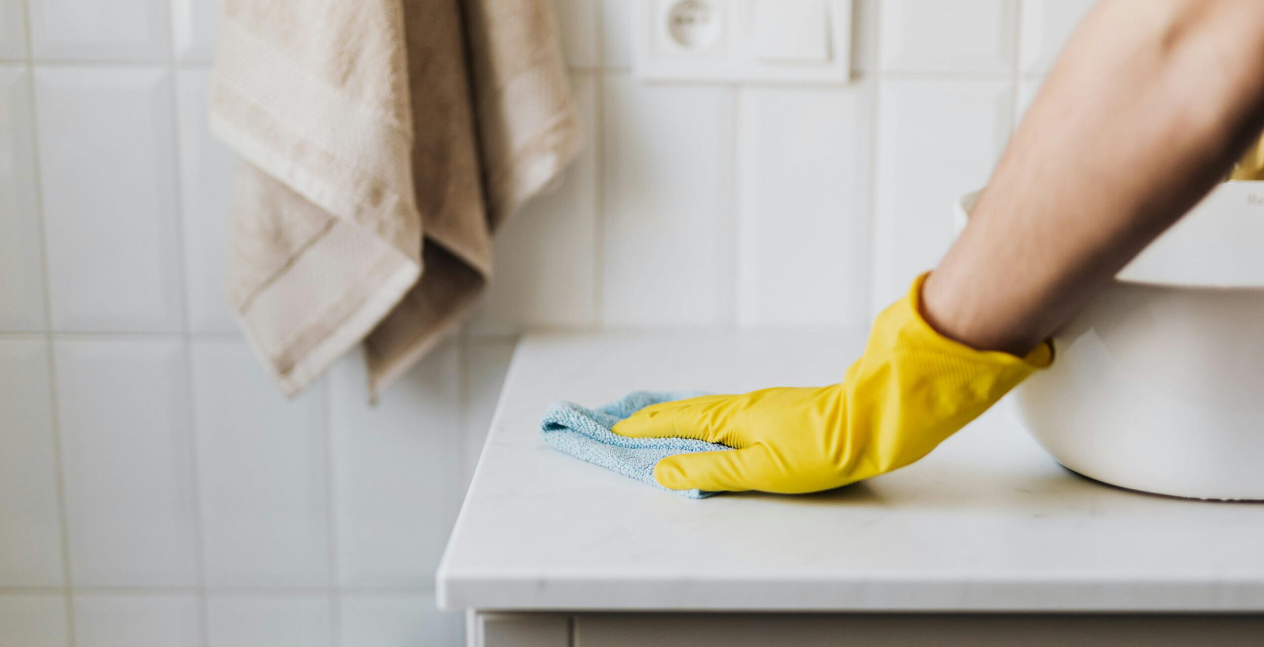 Main gantée effectuant le nettoyage d'une surface blanche dans une salle de bain.