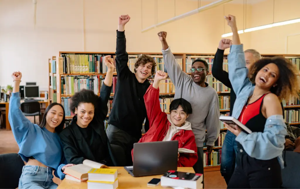 Groupe d'apprenants souriants célébrant leur réussite en formation dans une bibliothèque.